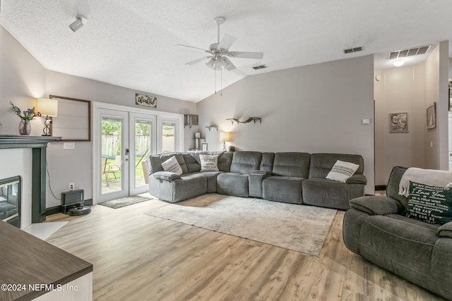 living room featuring ceiling fan, french doors, a textured ceiling, light wood-type flooring, and vaulted ceiling