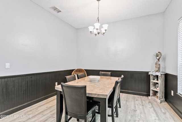 dining space featuring a textured ceiling, wood walls, an inviting chandelier, and light hardwood / wood-style flooring