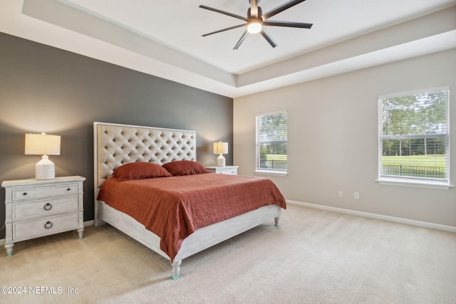 carpeted bedroom with ceiling fan and a tray ceiling