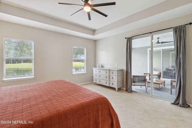 bedroom featuring ceiling fan, access to exterior, light carpet, and a tray ceiling