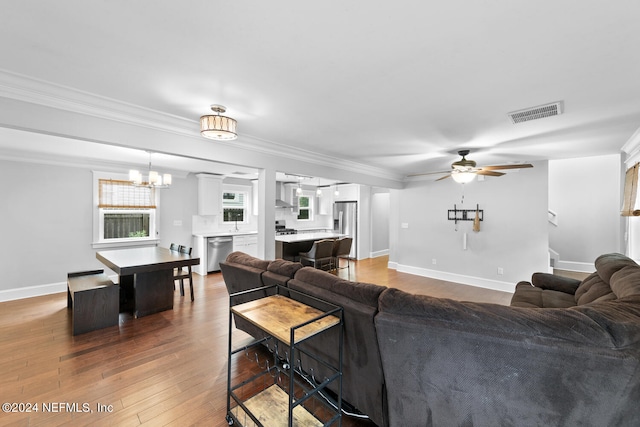 living room with ceiling fan with notable chandelier, wood-type flooring, and crown molding