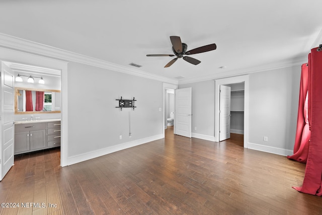 unfurnished bedroom with dark wood-type flooring, connected bathroom, ceiling fan, a walk in closet, and ornamental molding