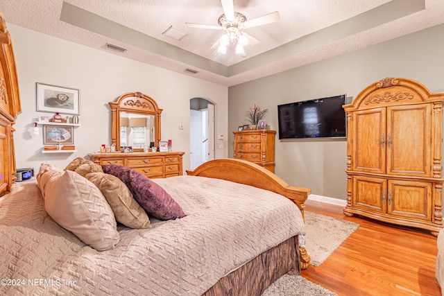 bedroom featuring a textured ceiling, ceiling fan, light wood-type flooring, and a tray ceiling