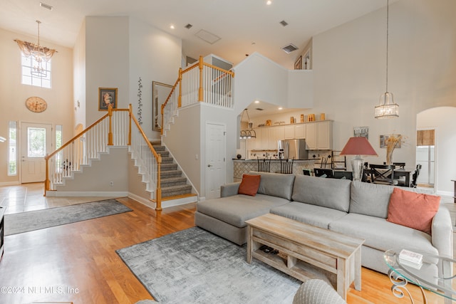 living room with light wood-type flooring, high vaulted ceiling, and a notable chandelier