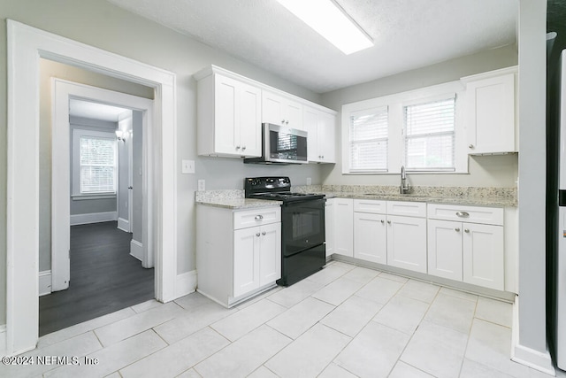 kitchen featuring light stone countertops, white cabinets, sink, black electric range oven, and light tile patterned flooring