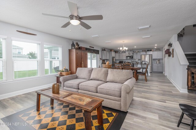 living room with ceiling fan with notable chandelier, light wood-type flooring, and a textured ceiling