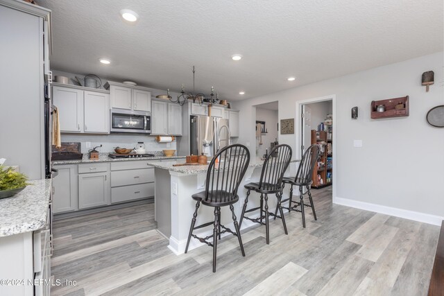 kitchen featuring light hardwood / wood-style floors, light stone counters, a kitchen island, stainless steel appliances, and a textured ceiling