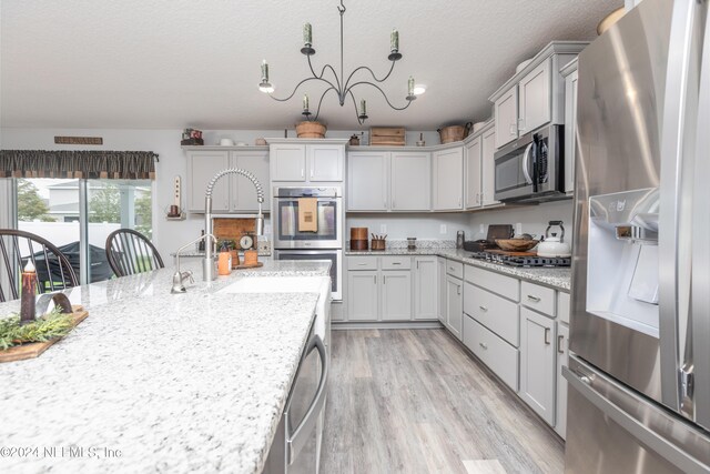 kitchen featuring light hardwood / wood-style floors, a notable chandelier, hanging light fixtures, appliances with stainless steel finishes, and light stone countertops