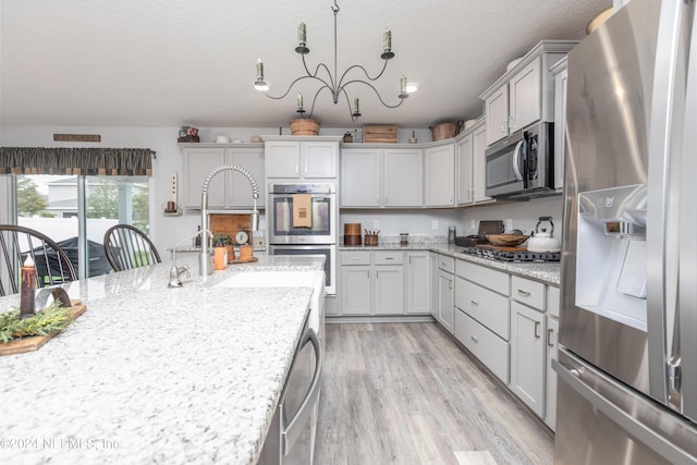243 Bluejack Ln, Saint Augustine, FL 32095 - kitchen with a notable chandelier, light wood-style flooring, light stone counters, a textured ceiling, and appliances with stainless steel finishes