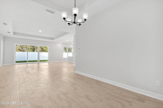 empty room with a chandelier, a raised ceiling, and light hardwood / wood-style floors