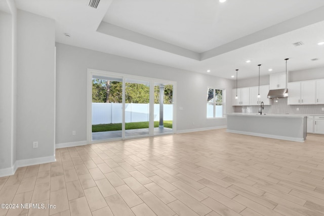 unfurnished living room featuring sink, a raised ceiling, a healthy amount of sunlight, and light hardwood / wood-style floors