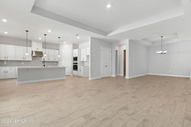 unfurnished living room featuring light hardwood / wood-style flooring, a raised ceiling, a notable chandelier, and sink