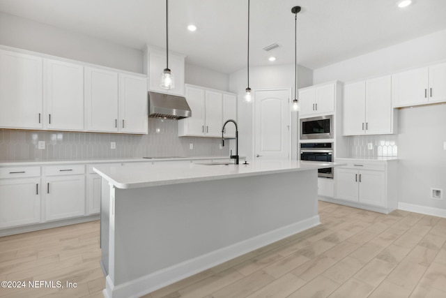 kitchen featuring appliances with stainless steel finishes, a center island with sink, white cabinets, light hardwood / wood-style floors, and hanging light fixtures