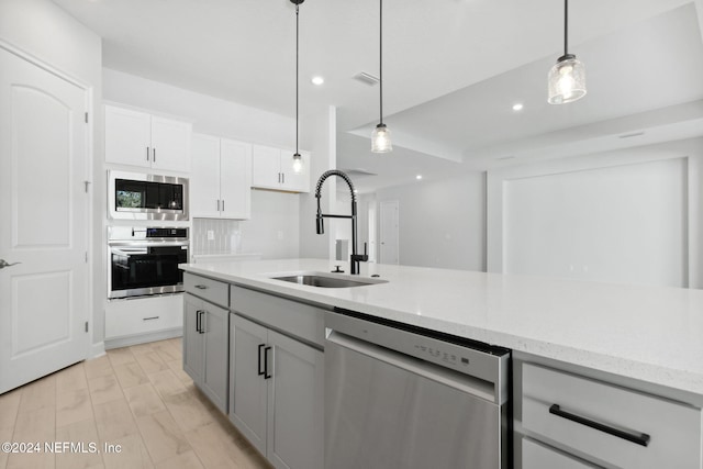 kitchen featuring stainless steel appliances, sink, pendant lighting, white cabinets, and light hardwood / wood-style floors