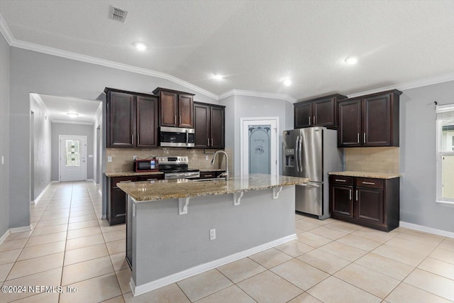 kitchen featuring a textured ceiling, vaulted ceiling, a kitchen breakfast bar, appliances with stainless steel finishes, and an island with sink