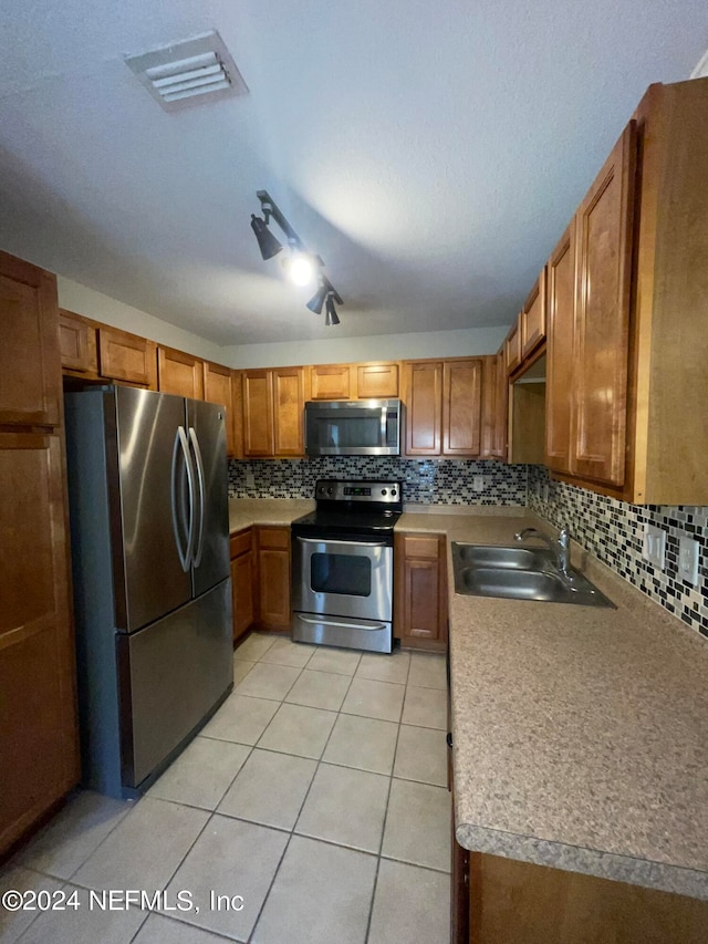 kitchen with appliances with stainless steel finishes, light tile patterned floors, sink, and decorative backsplash