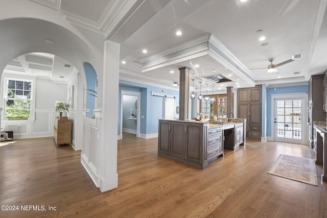 kitchen featuring ceiling fan, ornamental molding, a center island with sink, dark wood-type flooring, and decorative columns