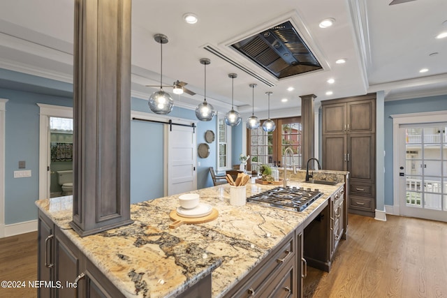 kitchen with a large island with sink, light stone counters, a barn door, ornate columns, and wood-type flooring