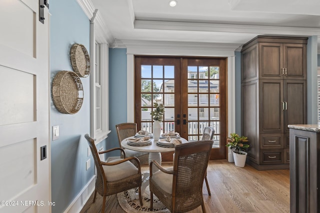 dining space with a barn door, ornamental molding, light wood-type flooring, and french doors