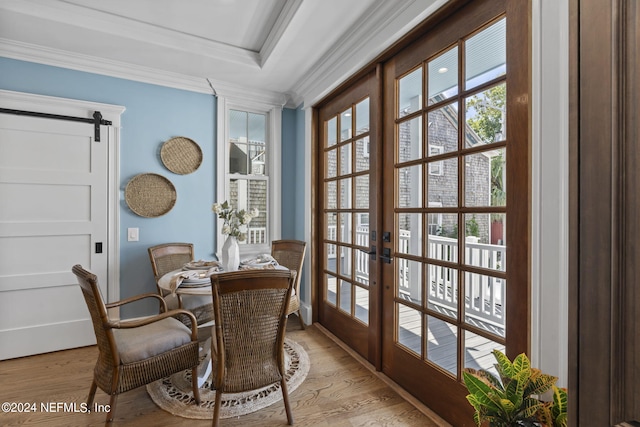 dining room featuring a barn door, a raised ceiling, light wood-type flooring, crown molding, and french doors