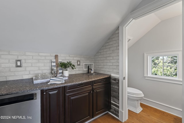 kitchen featuring dark stone counters, light hardwood / wood-style floors, lofted ceiling, dark brown cabinetry, and stainless steel dishwasher