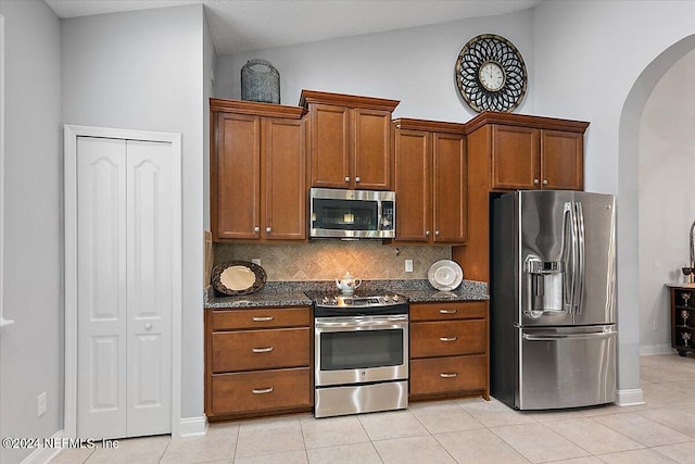 kitchen featuring vaulted ceiling, appliances with stainless steel finishes, dark stone counters, light tile patterned flooring, and tasteful backsplash