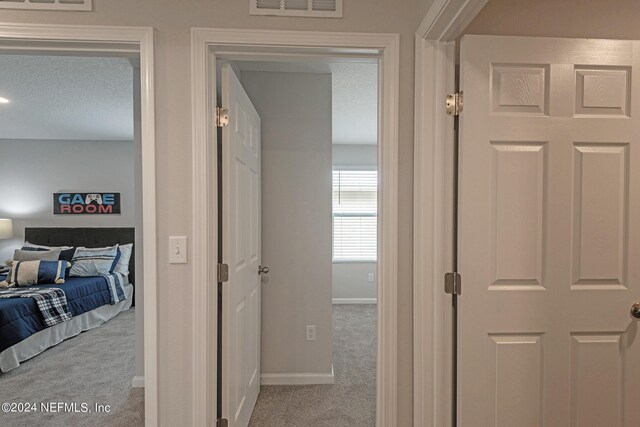 hallway with light colored carpet and a textured ceiling