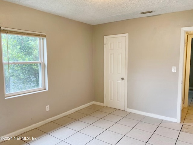 tiled spare room with a textured ceiling and a healthy amount of sunlight