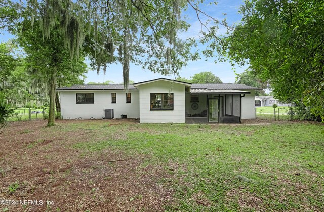 back of property with a sunroom, a yard, and central AC