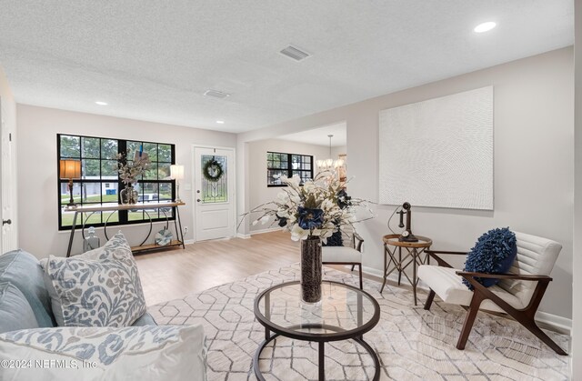 living room with an inviting chandelier, light hardwood / wood-style floors, and a textured ceiling