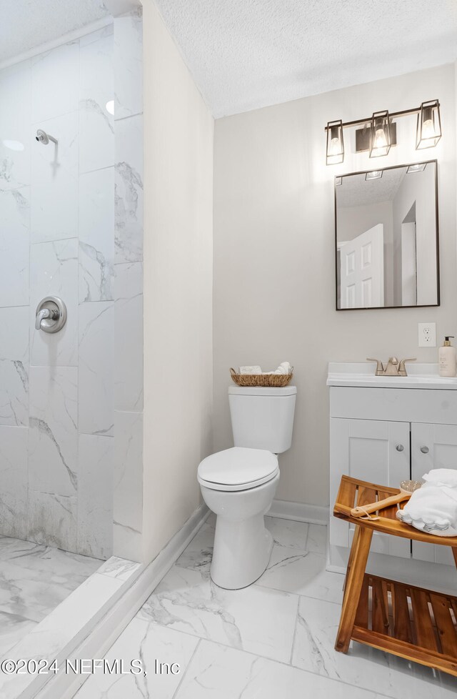 bathroom with a textured ceiling, vanity, toilet, and a tile shower