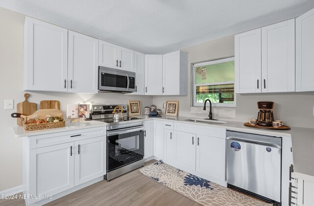 kitchen with light wood-type flooring, stainless steel appliances, white cabinetry, sink, and a textured ceiling