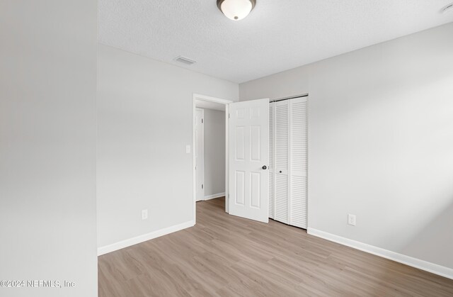 unfurnished bedroom with a closet, a textured ceiling, and light hardwood / wood-style flooring