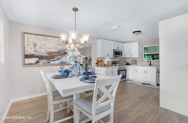 dining space featuring a textured ceiling, light hardwood / wood-style flooring, an inviting chandelier, and sink