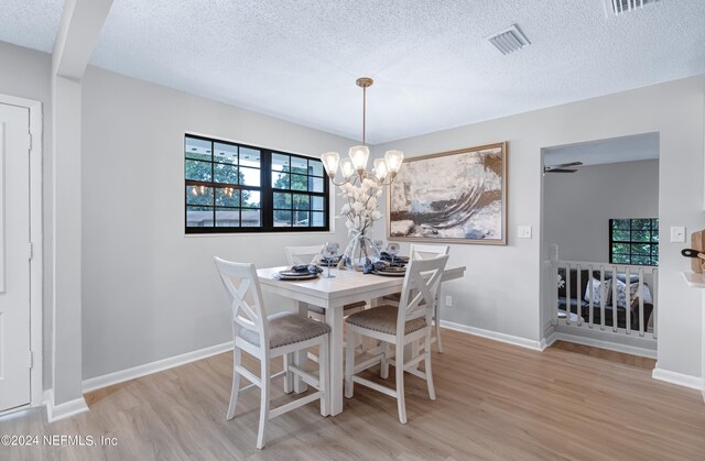 dining area with ceiling fan with notable chandelier, a textured ceiling, a healthy amount of sunlight, and light hardwood / wood-style flooring