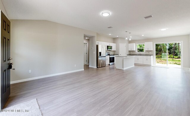 unfurnished living room with a textured ceiling, light wood-type flooring, sink, and vaulted ceiling