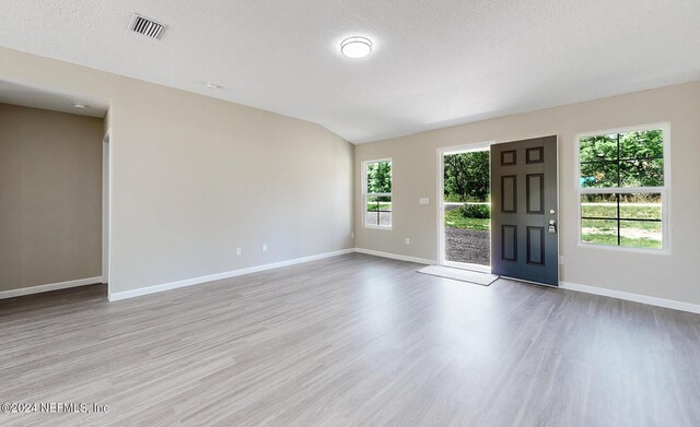 unfurnished room featuring a textured ceiling, vaulted ceiling, and light hardwood / wood-style flooring