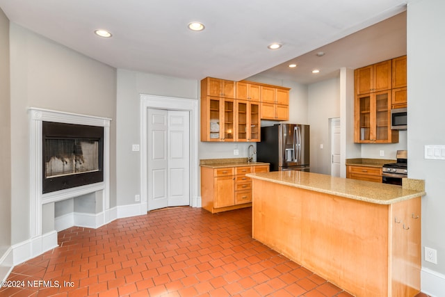 kitchen featuring kitchen peninsula, light stone counters, stainless steel appliances, sink, and a fireplace