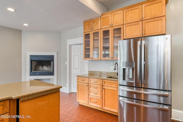 kitchen with stainless steel refrigerator with ice dispenser, light stone counters, and sink