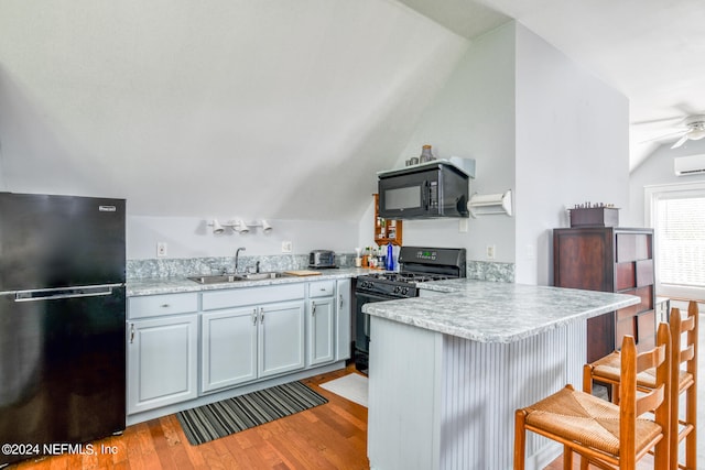 kitchen with sink, a kitchen breakfast bar, kitchen peninsula, lofted ceiling, and black appliances