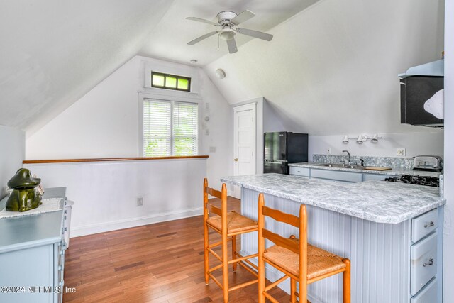 kitchen featuring a kitchen breakfast bar, black fridge, vaulted ceiling, hardwood / wood-style flooring, and ceiling fan