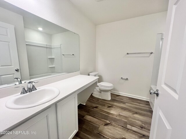 bathroom featuring vanity, wood finished floors, baseboards, a shower, and toilet