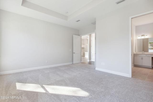 unfurnished bedroom with light carpet, a raised ceiling, ensuite bath, and sink