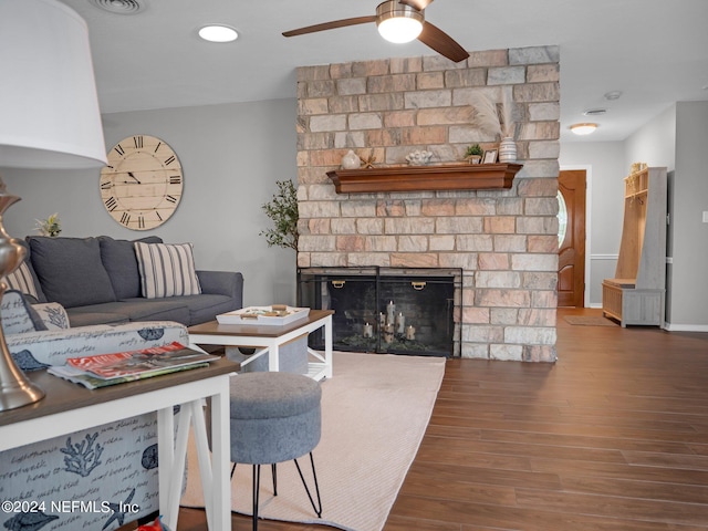 living room featuring ceiling fan, hardwood / wood-style floors, and a stone fireplace