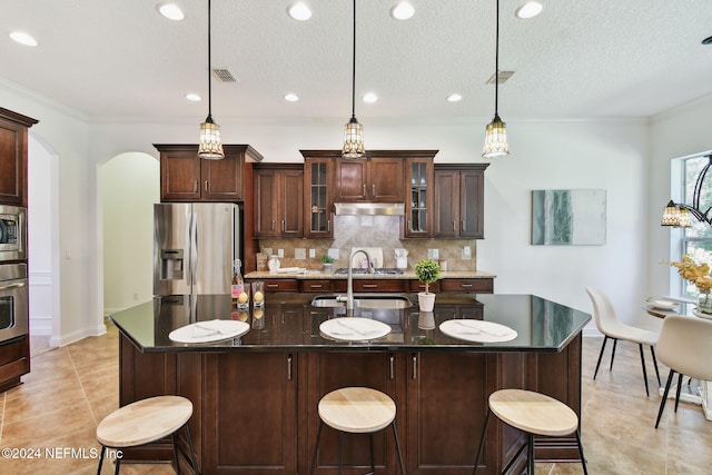 kitchen with decorative light fixtures, stainless steel appliances, and an island with sink