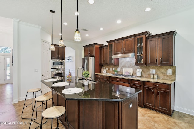 kitchen with decorative backsplash, stainless steel appliances, a kitchen island with sink, sink, and decorative light fixtures