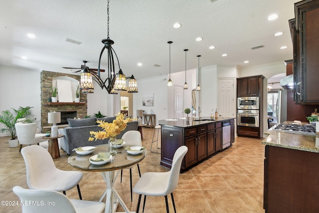 kitchen featuring dark brown cabinets, stainless steel appliances, decorative light fixtures, a fireplace, and an island with sink