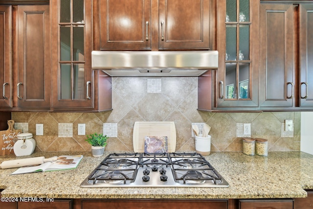 kitchen featuring stainless steel gas stovetop, light stone counters, backsplash, and extractor fan