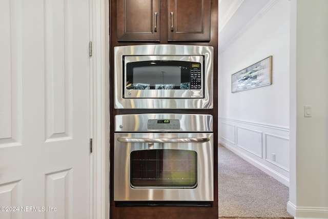 kitchen featuring ornamental molding, dark brown cabinetry, stainless steel appliances, and carpet floors