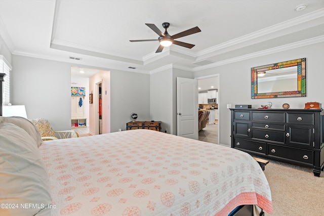 carpeted bedroom featuring a tray ceiling, ornamental molding, connected bathroom, and ceiling fan